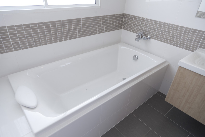 Bathroom with acrylic tub, tiled wall, and flooring