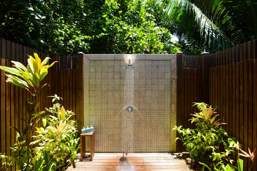 Beach house style outdoor shower with tile wall, wood fence, and plants