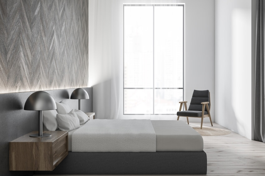 Bedroom with white and wooden walls, gray bed and armchair, and a floating wooden table
