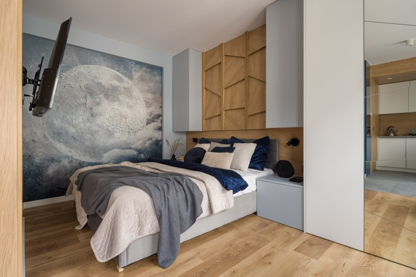 Bedroom with mural wallpaper, open shelf, and wood flooring