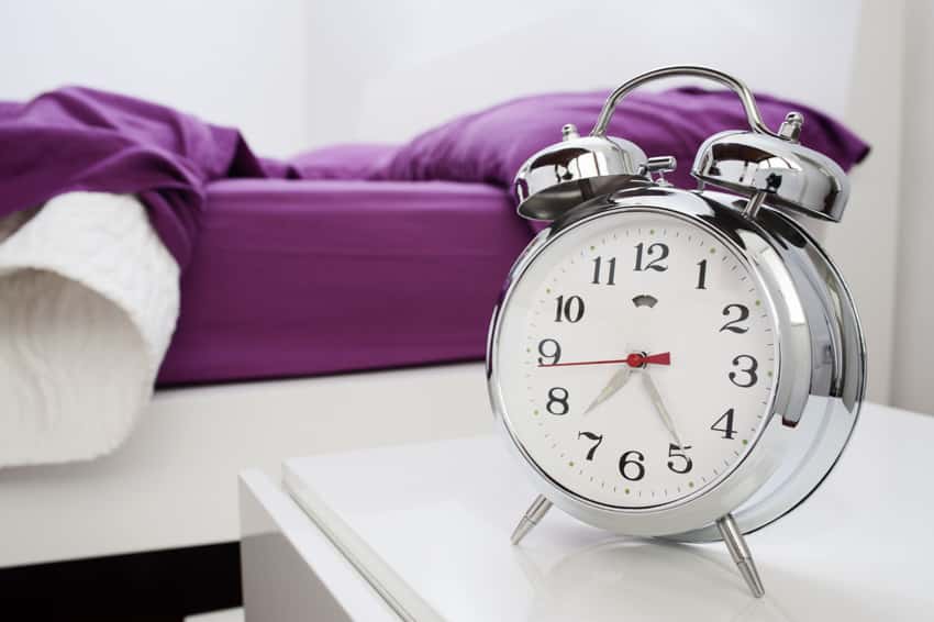 Bedroom with purple bedsheet, a nightstand and alarm clock