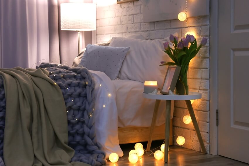 Bedroom with romantic lighting, cozy bed, brick wall, and flowers on side table