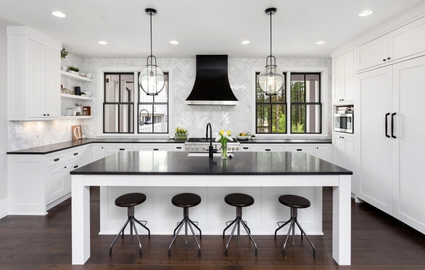 Black and white kitchen with large island, herringbone tile backsplash, and cabinets with black hardware
