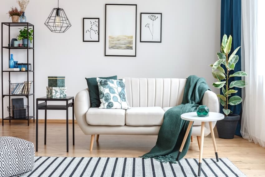 Black steel table next to sofa in cozy apartment interior with gallery of posters and stripe carpet