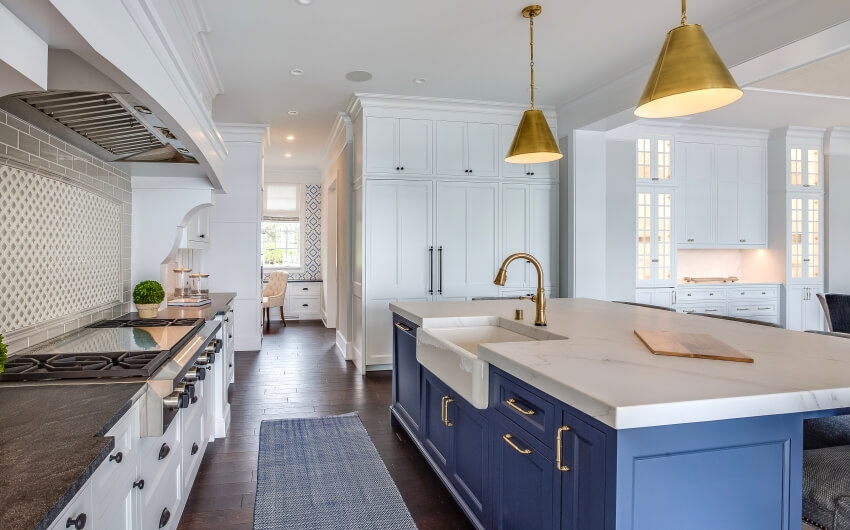 Blue island with brushed gold pendant lights in a kitchen with dark hardwood floors and mixed countertops