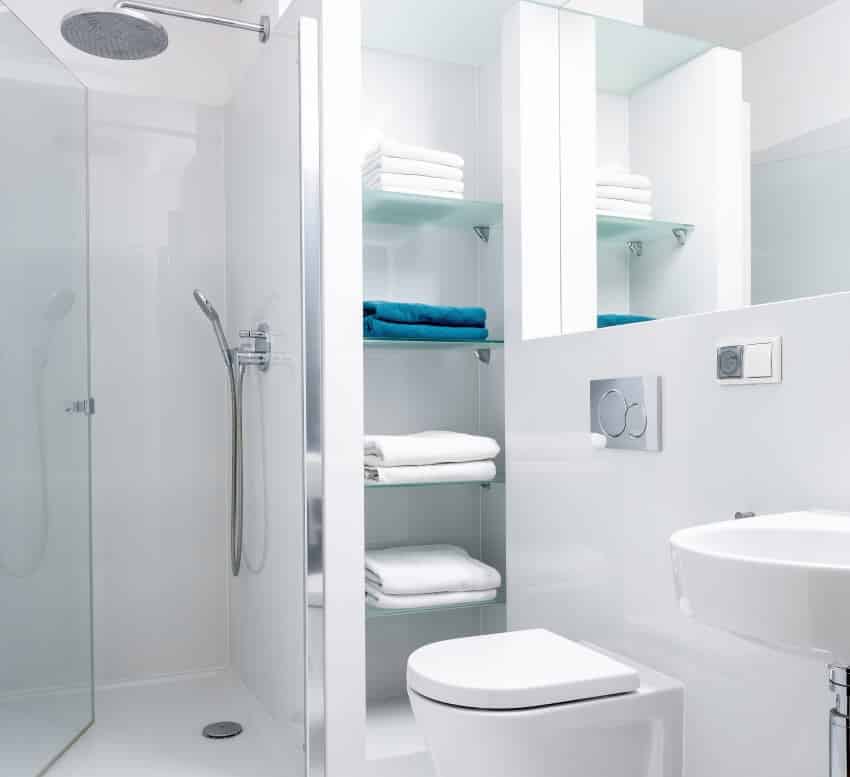 Bright white bathroom with shower shelves and mirror above toilet and sink