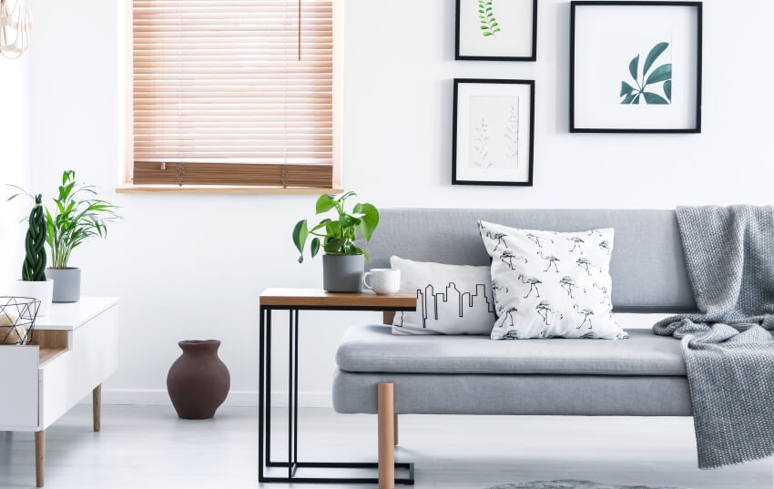 C-type sofa table beside grey couch with cushions and blanket in white sitting room interior with poster