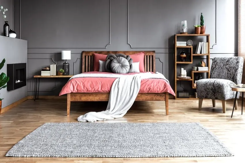 Carpet runner in spacious grey and pink bedroom interior with wooden bed and patterned armchair