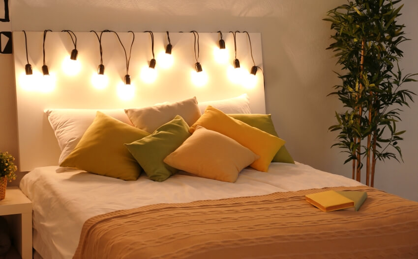 Comfortable double bed in a bedroom with cozy fairy lights on headboard and plant on the side