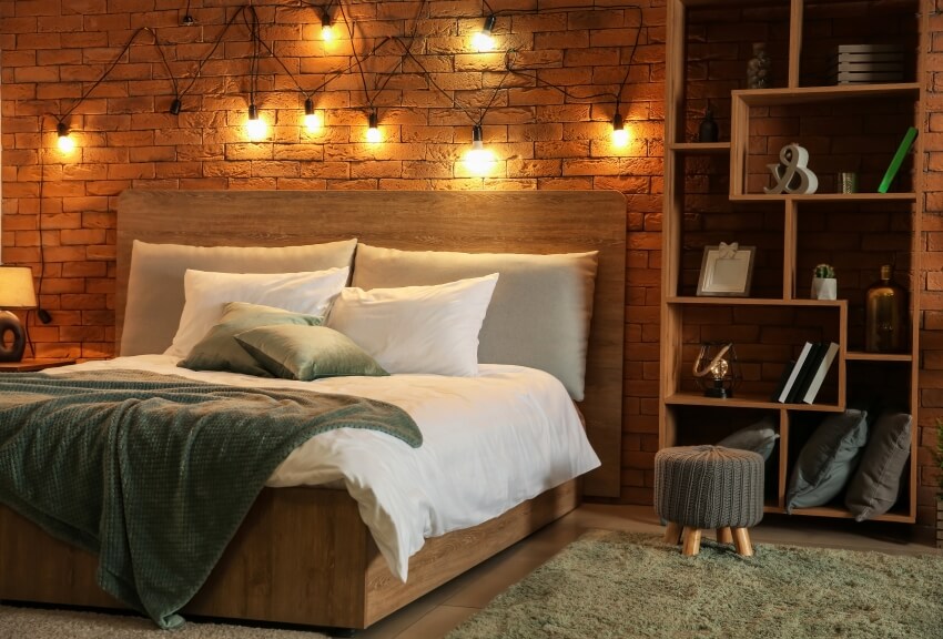 Comfortable wooden bed, wood shelves, footstool, and mood lighting on a brick wall in a bedroom