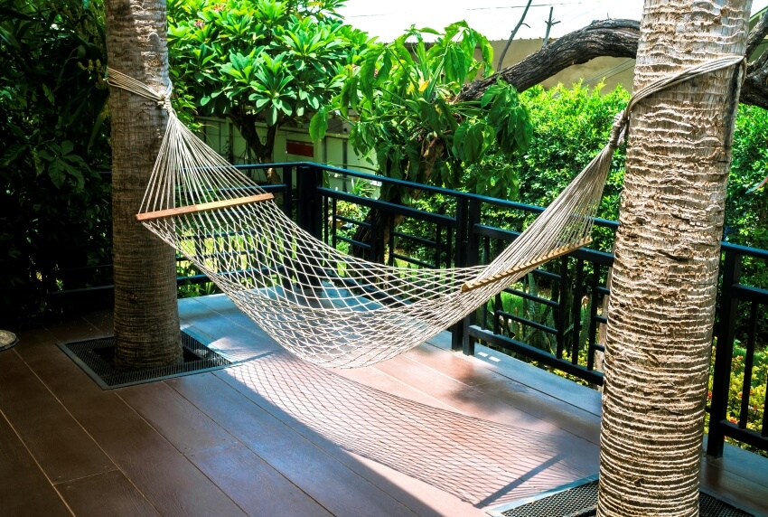 Cotton rope hammock in between twO trees at the wooden terrace near outdoor garden