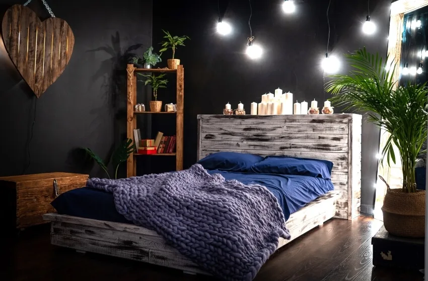 Dark bedroom with black walls, wood furniture, candles on headboard, and romantic mood lighting