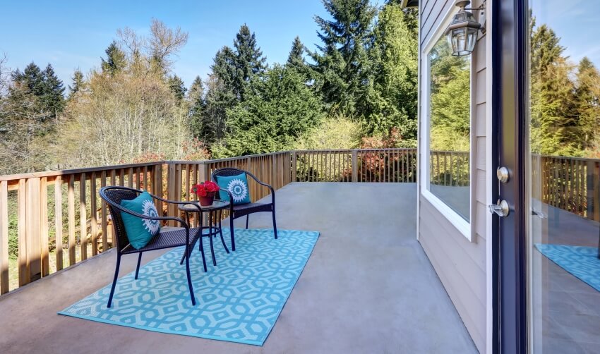Deck with wooden railings and outdoor chairs accented with blue pillows on patterned runner rug