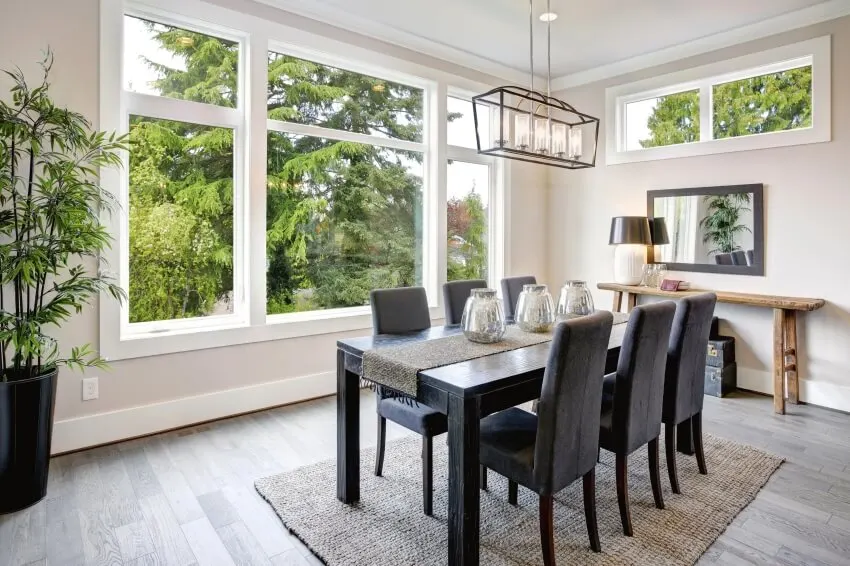Dining room with black dining table, grey velvet chairs over taupe sisal runner rug, and large windows