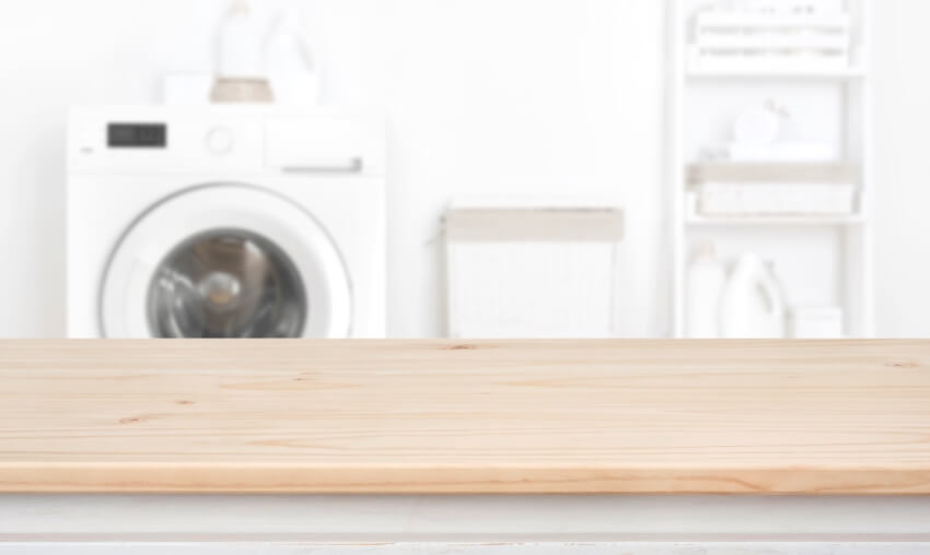 Empty Wooden table over blurred laundry room washing machine background