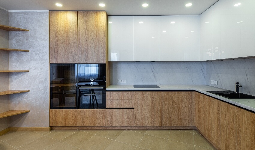 Empty apartment kitchen with built-in appliances, corner floating shelves, and wood laminate cabinets