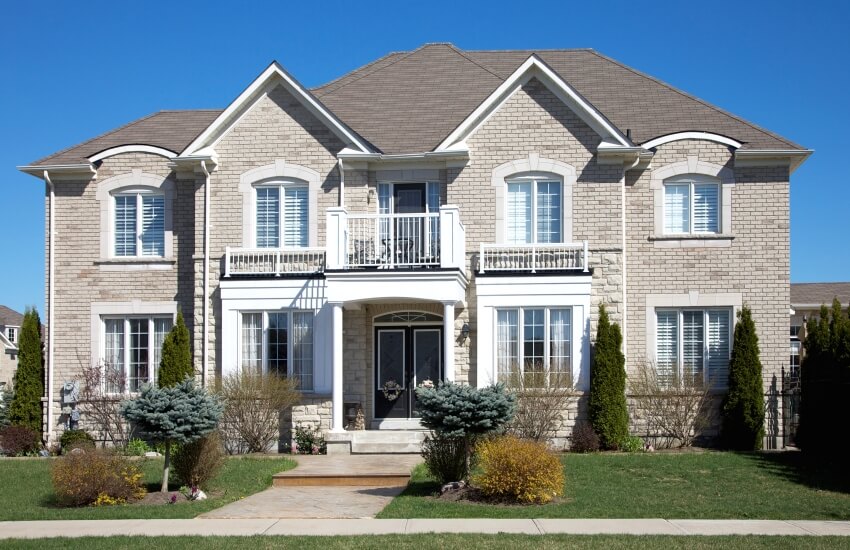 Facade of a modern home with painted brick exterior, balcony, and porch with columns