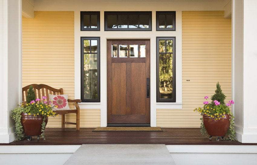 Front porch with light yellow siding, front door, wood floor, chair, and potted plants