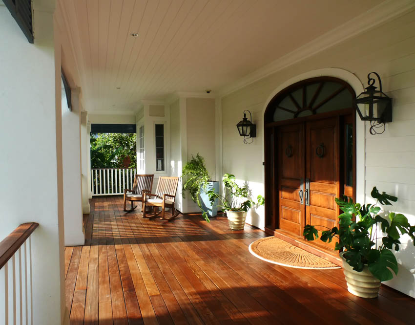 Front porch with wood flooring, door, wall mounted lamps, and potted plants