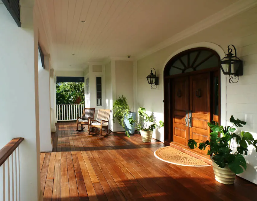 porch with light green paint, plank flooring, door, wall mounted lamps, and potted plants