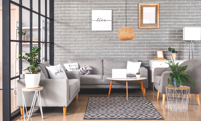 Grey interior of living room with brick wall, sofa, end table, and pendant lights
