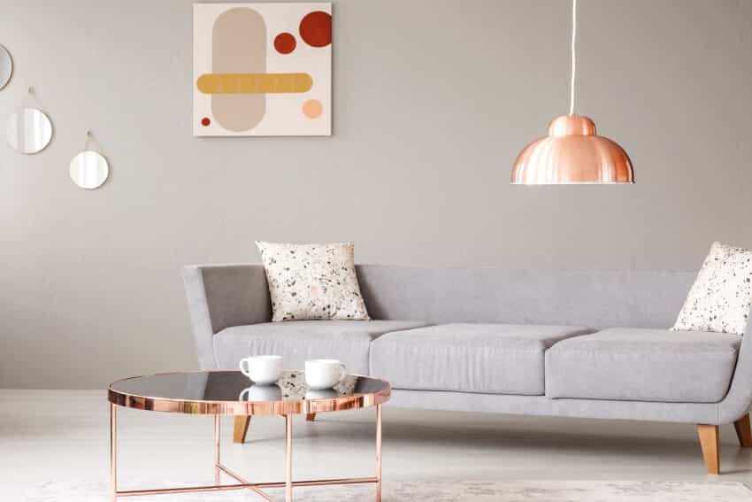 Grey sofa, painting on a wall, glass coffee table, and copper lamp in a living room interior