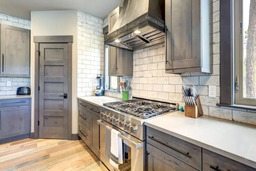 Grey tone kitchen interior with brick backsplash, wood floor, and stainless steel appliance