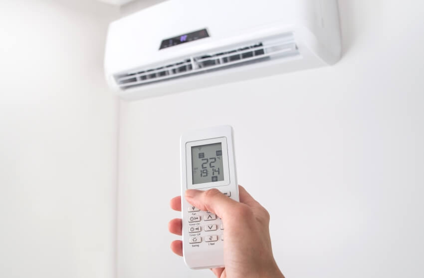 Hand holding remote control adjusting temperature of air conditioner mounted on a white wall
