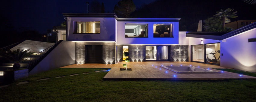 House exterior with color changing landscape lights, deck, glass windows, and doors