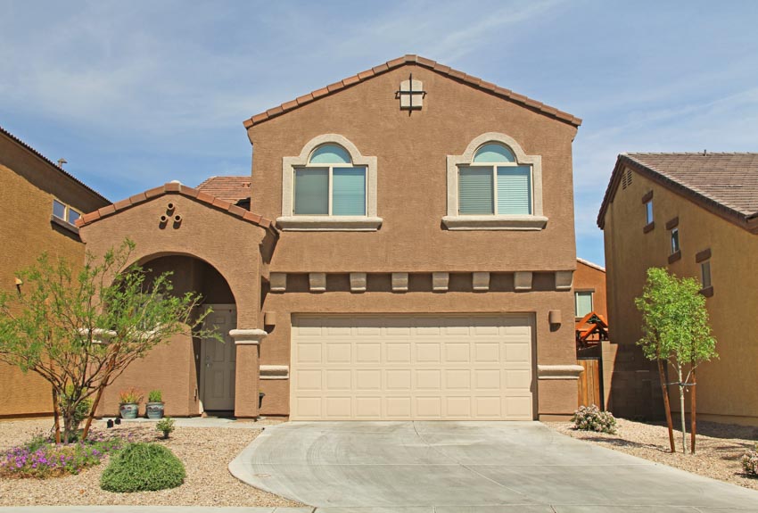 House exterior with garage door, painting stucco pros and cons, driveway, and windows