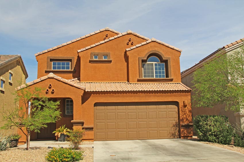 House exterior with painting stucco pros and cons, garage driveway, and windows