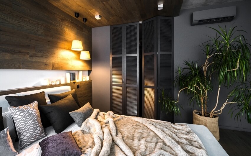 Interior of a stylish bedroom with a black wardrobe, wooden walls, dark linens, and warm yellow lighting