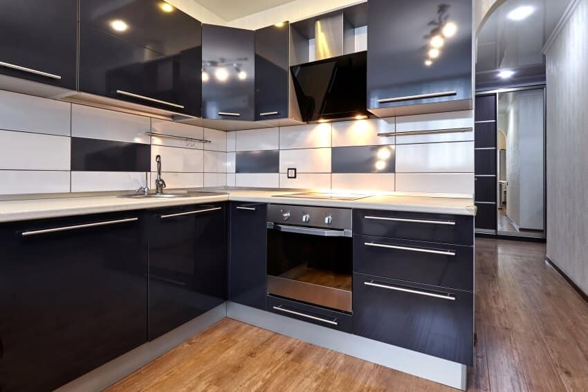 Kitchen interior with tile backsplash, high gloss black cabinets, and wood floor