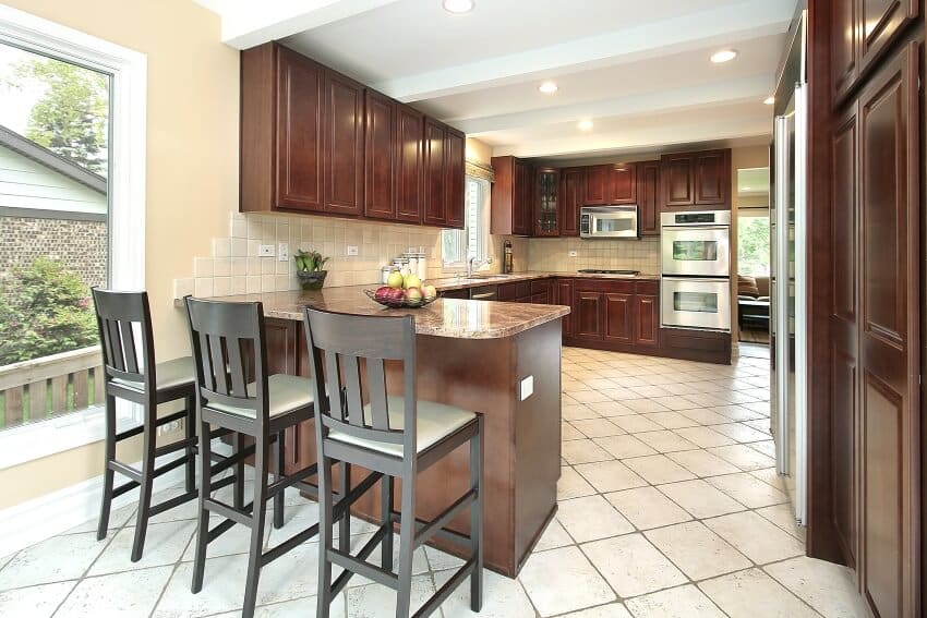 Kitchen with ceiling beams, tile floor, dark wood cabinets, and breakfast bar with brown granite countertop