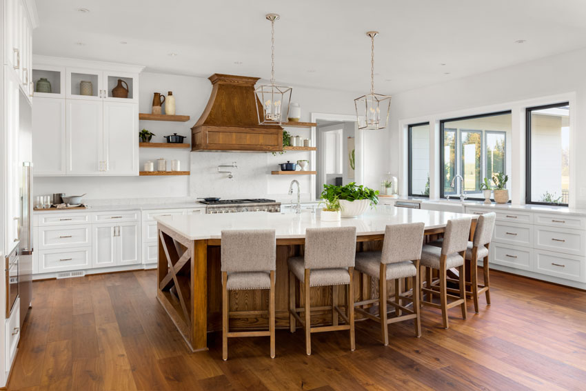 Kitchen with center island, dining area, white cabinets, wood floors, range hood, windows, and pendant lights
