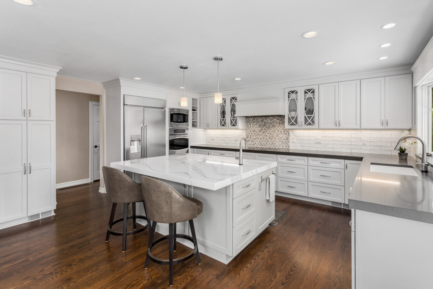 Kitchen with center island, white cabinets, chairs, wood flooring, and recessed lighting