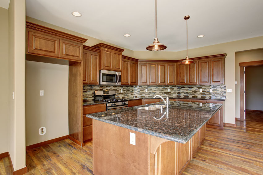 Kitchen with overhang countertop, paneled island, cabinets, and brown glass backsplash