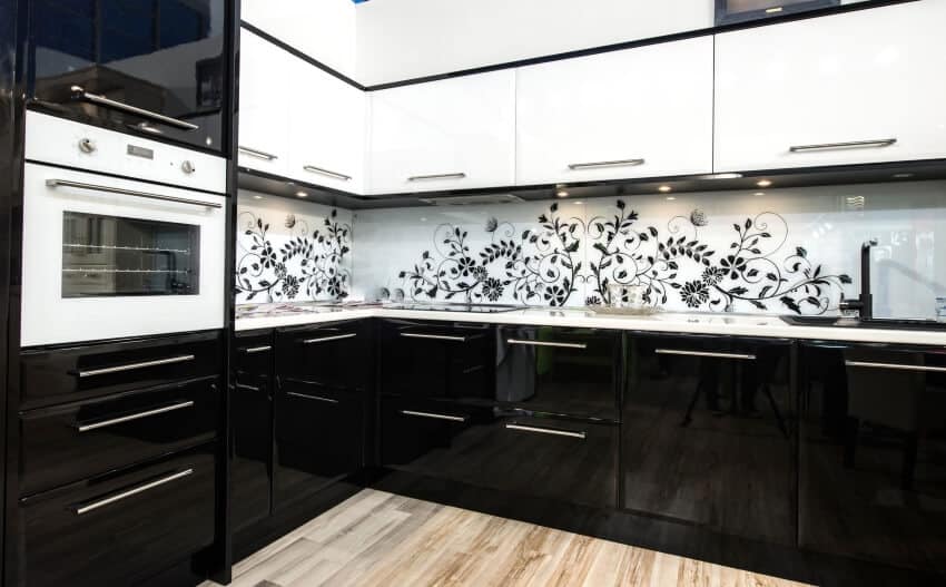 Kitchen with glossy black and white cabinets, and flower painted tile backsplash