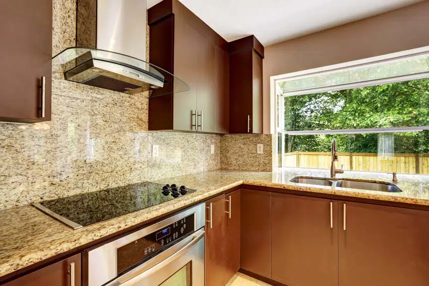 Kitchen with granite backsplash, brown cabinets, countertop, stove, range hood, sink, and windows