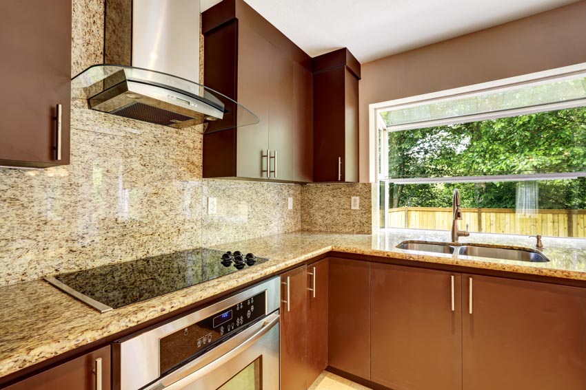 Kitchen with granite backsplash, counter, range hood, cabinets and window