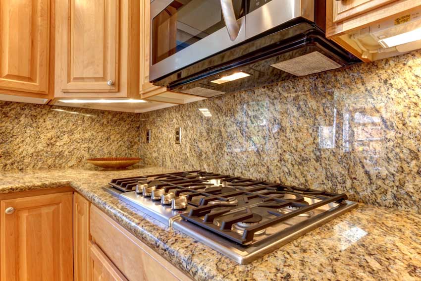 Kitchen with granite backsplash, countertop, stove, range hood, and cabinets