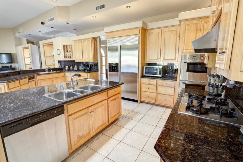 Kitchen with granite countertops, backsplash, wood cabinets, tile flooring, center island, sink, and faucet