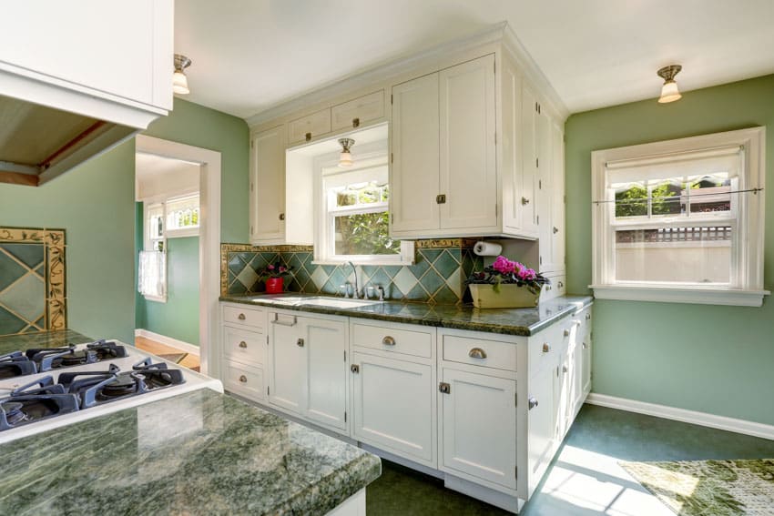 Kitchen with green marble countertop, white cabinets, and windows