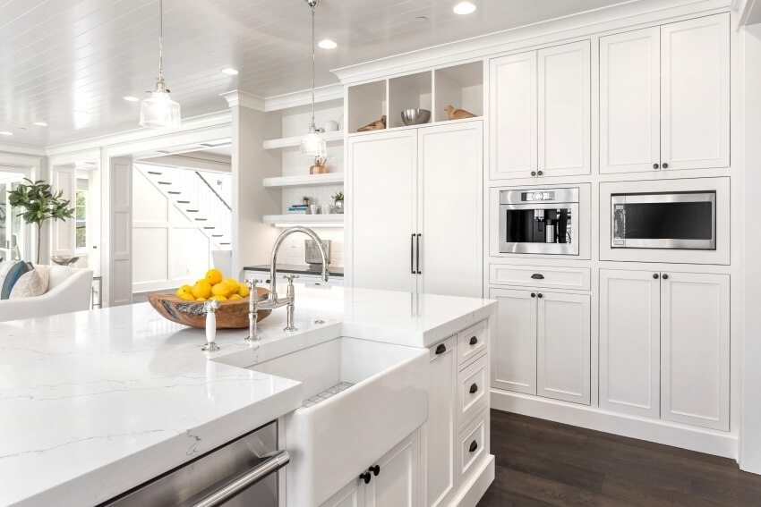 Kitchen with white cabinets, pendant lights, and island with marble countertop and farmhouse sink