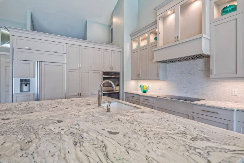Kitchen with white leathered quartzite countertop, island, cabinets, and backsplash