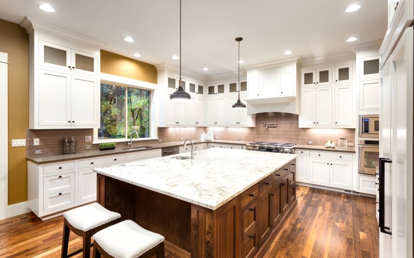 Large kitchen interior with island, white cabinets, mixed countertops, and hardwood floors