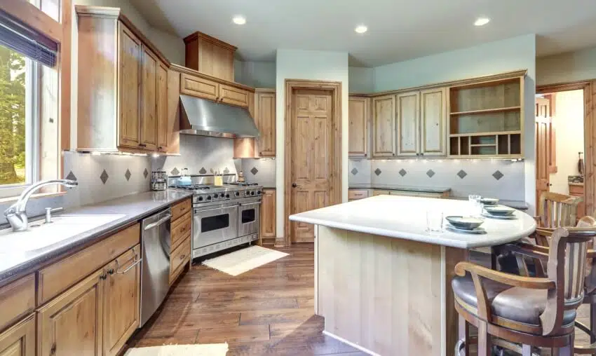 Large wooden kitchen with hardwood floors, acrylic countertops, and island with three chairs