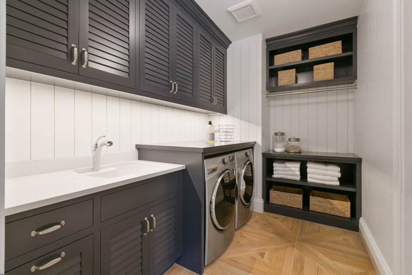 Laundry room with farmhouse style backsplash, cabinets, countertop, and washing machines