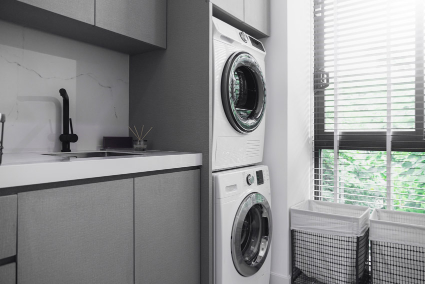 Laundry room with stacked laundry machines, laminate backsplash, countertop, and windows