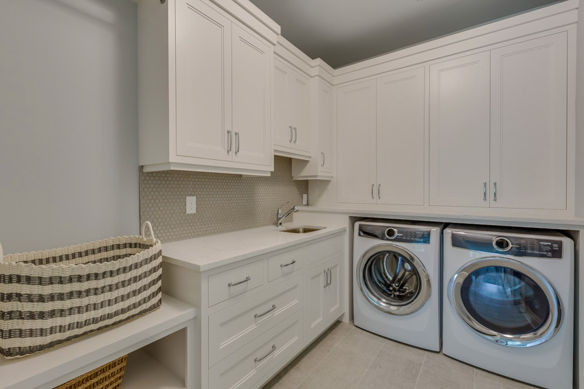 Laundry room with white cabinets, mosaic tile backsplash, and washing machines